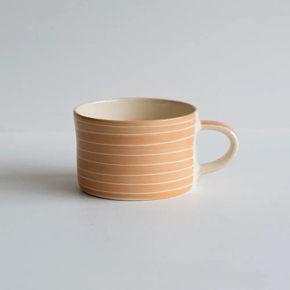 A ceramic mug with peach and white striped against a white backdrop.