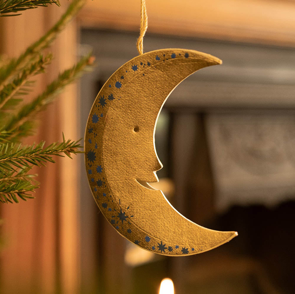 Decorative gold crescent moon ornament with star patterns hanging against a warm-toned background.
