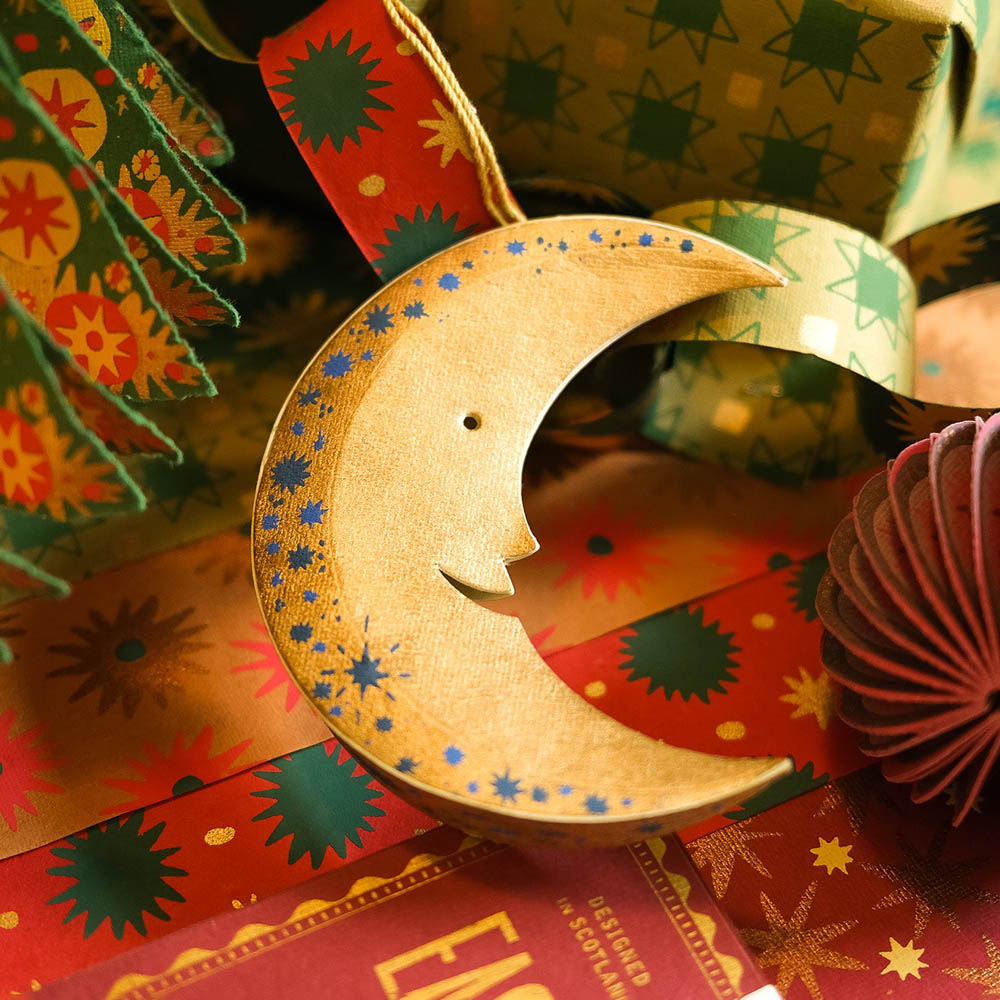 Wooden crescent moon ornament on a colorful background with gift wrap and decorative items.