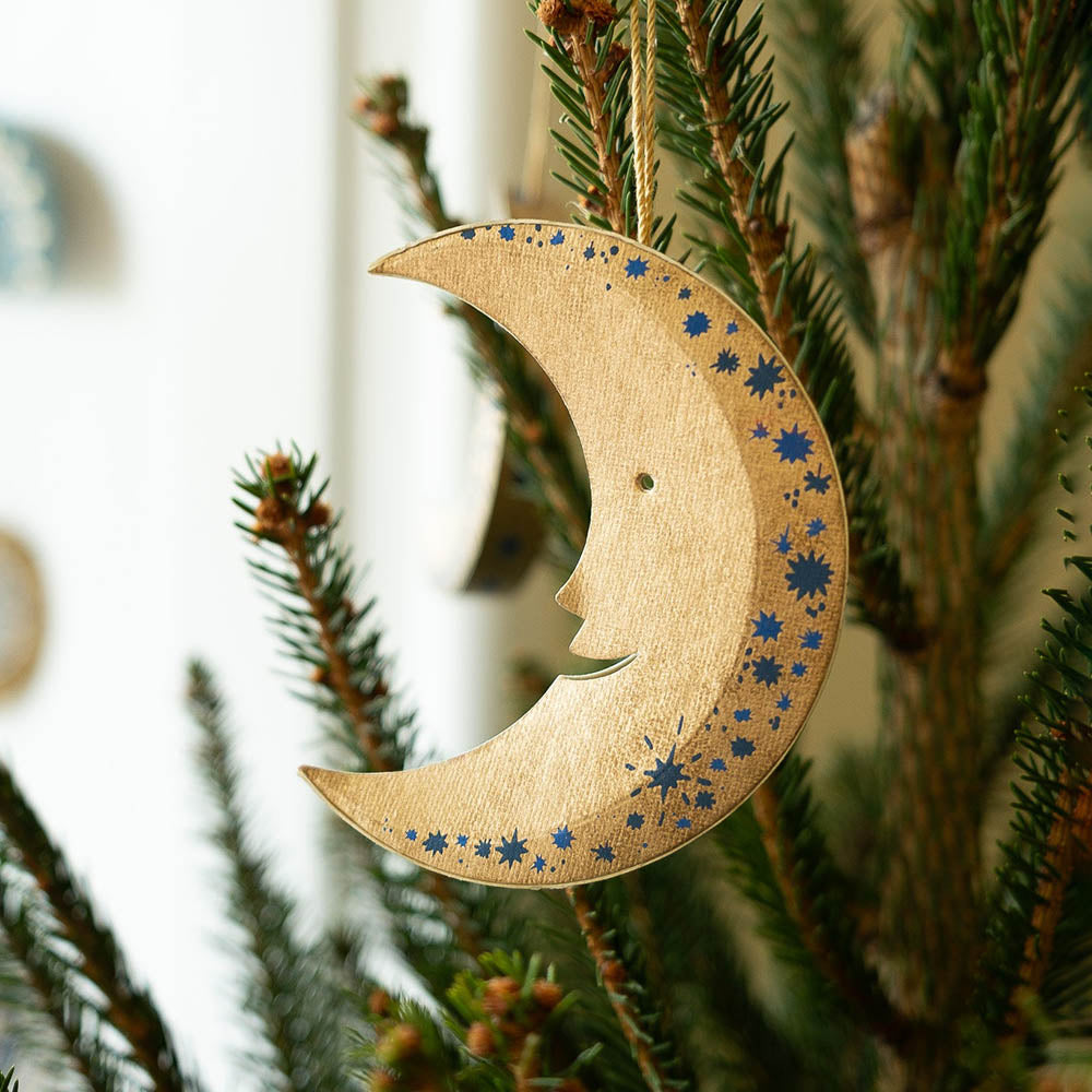 Wooden moon-shaped ornament with star patterns hanging on a Christmas tree.