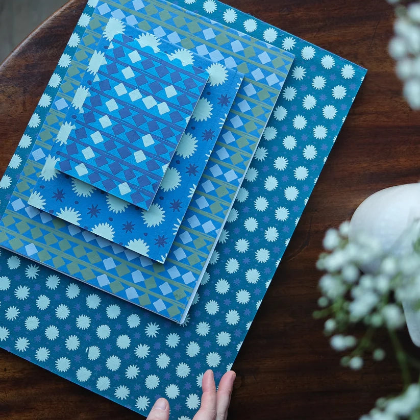 A selection of notebooks in different sizes stacked on top of each other. Each are blue with varying repeat patterns.