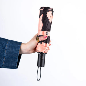 Hand holding a black and rose gold umbrella on a white background