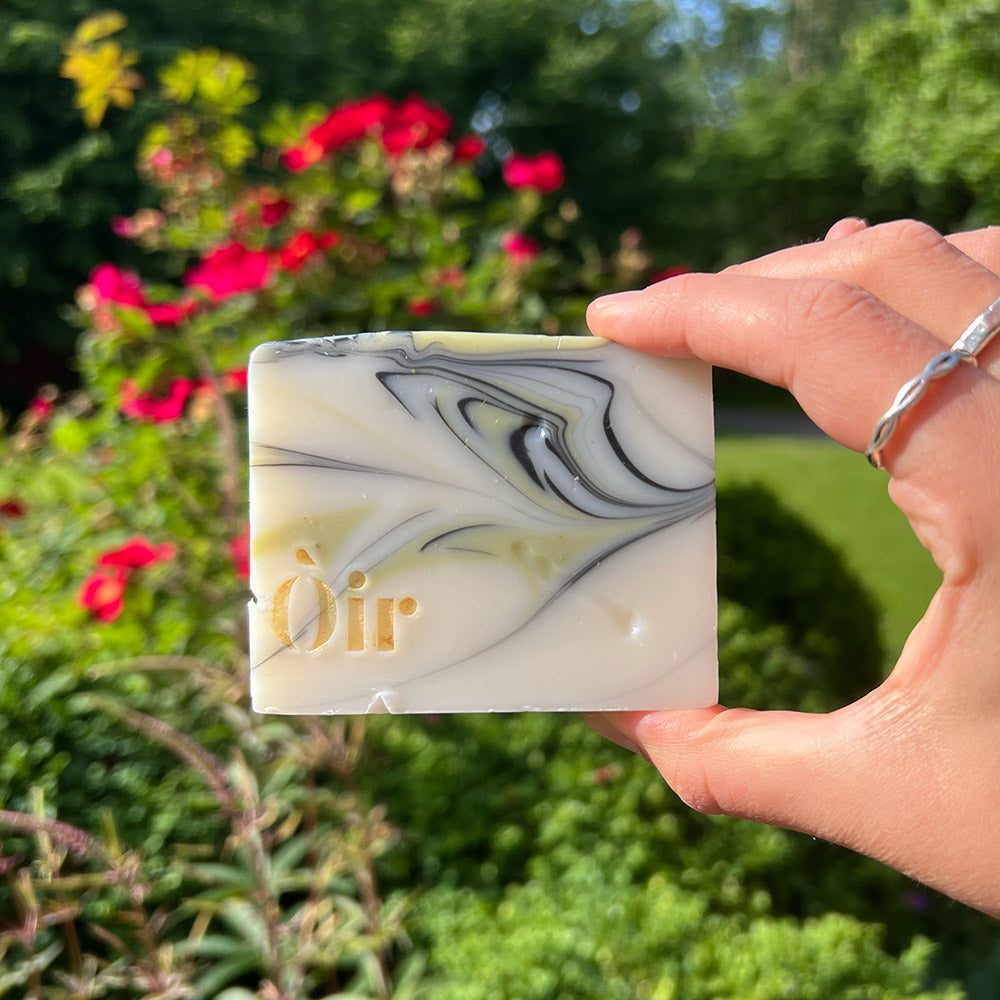 A person holding up a bar of soap in front of some foliage
