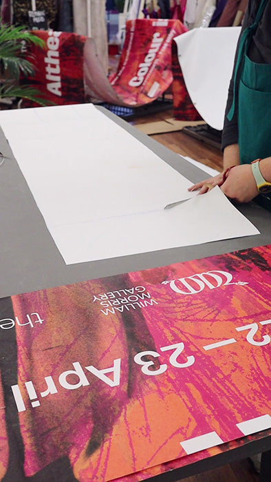 A person cutting up the reverse of an exhibition banner, against a work surface,