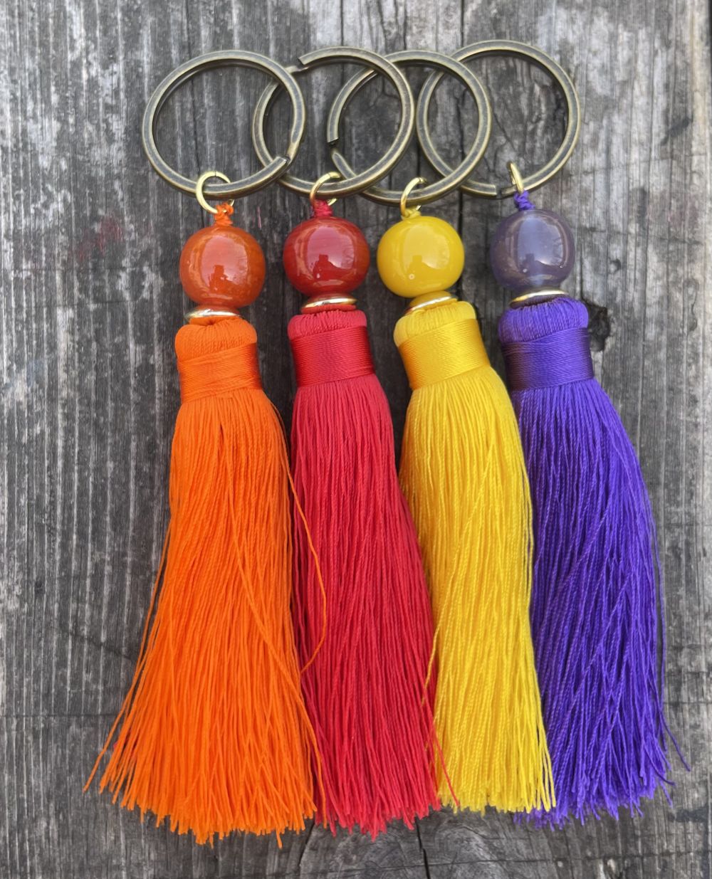 Four keychains with colorful tassels on a wooden surface