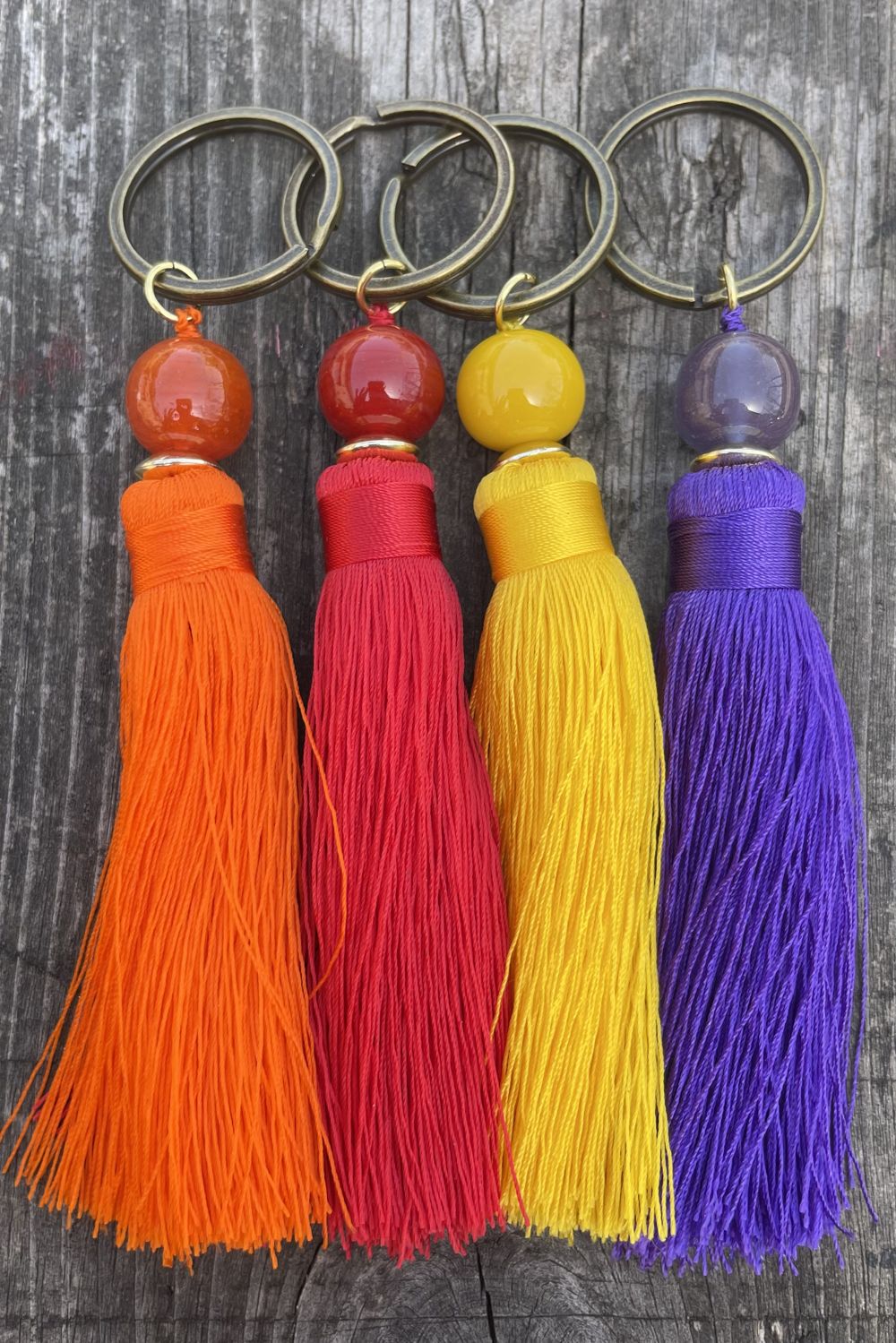Four colorful tassel keychains on a wooden surface