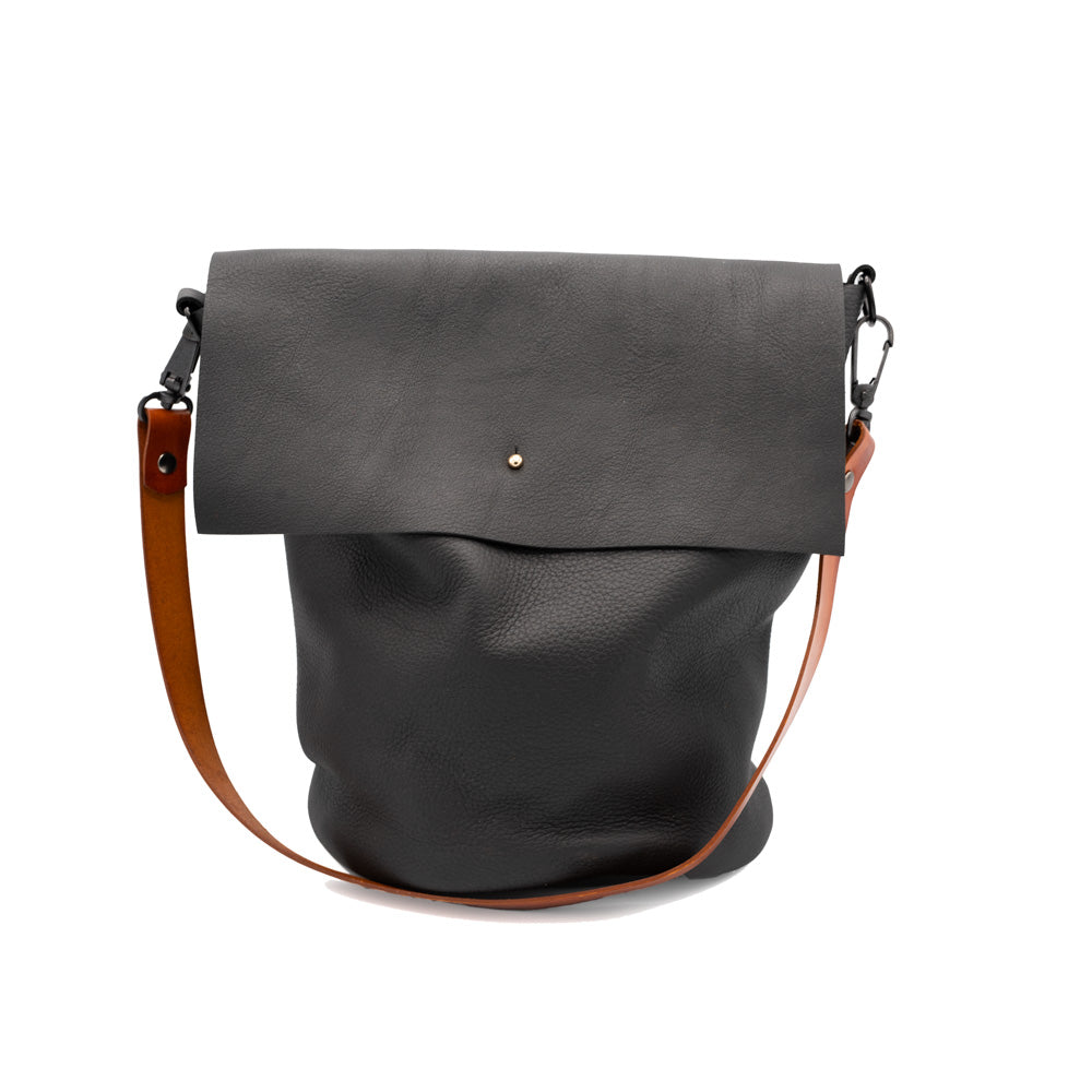 Black leather bucket bag with brown strap and stud closure. Photogarphed against a white backdrop.