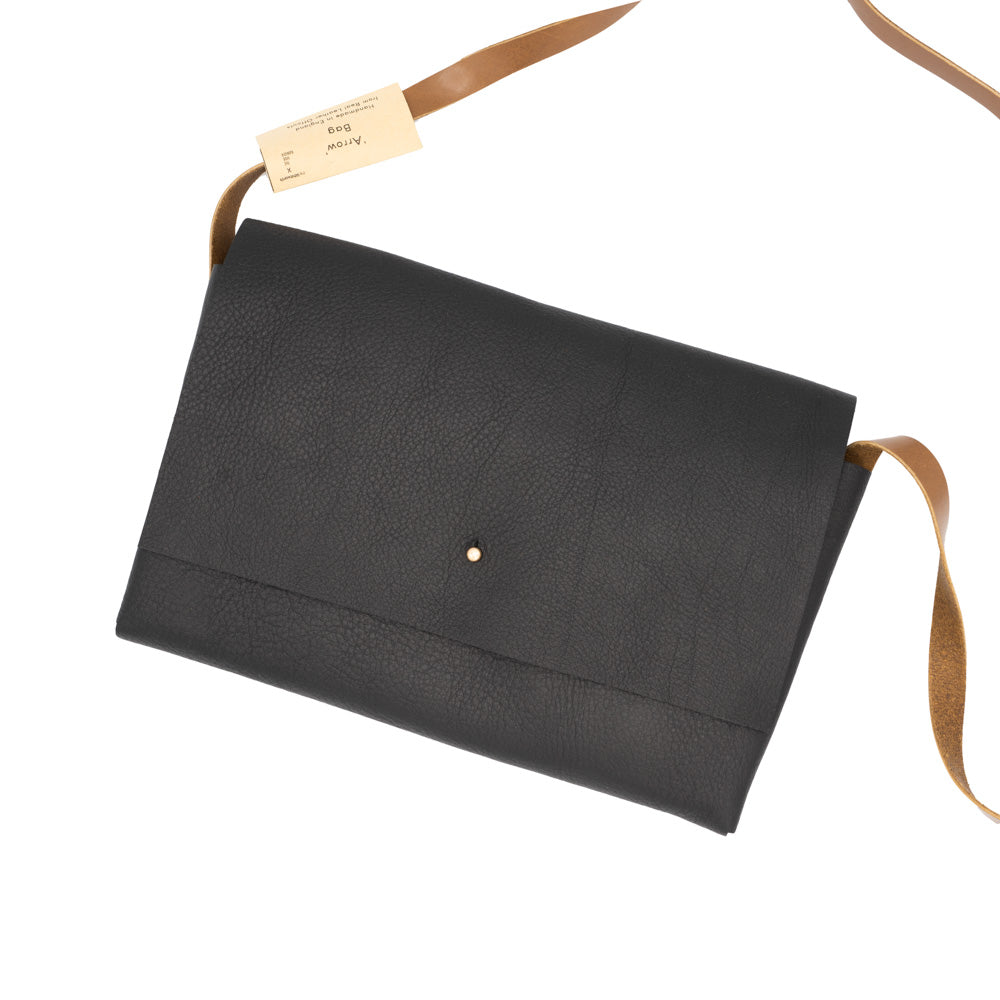 Rectangular-shaped black leather bag with stud closure, photographed against a white background. Brown tan strap partly framed in the shot.