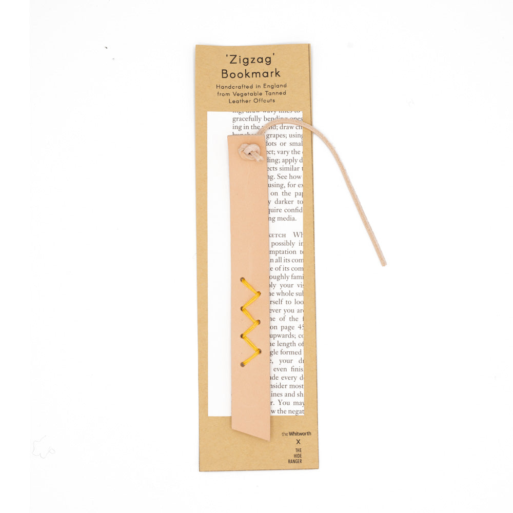 Pale pink leather bookmark with yellow zig-zag stitch detail. Photographed against backing card with information about the product. White background.