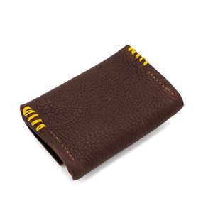 Rectangular brown leather purse with stud enclosure and yellow stitched detail photographed against a white background.
