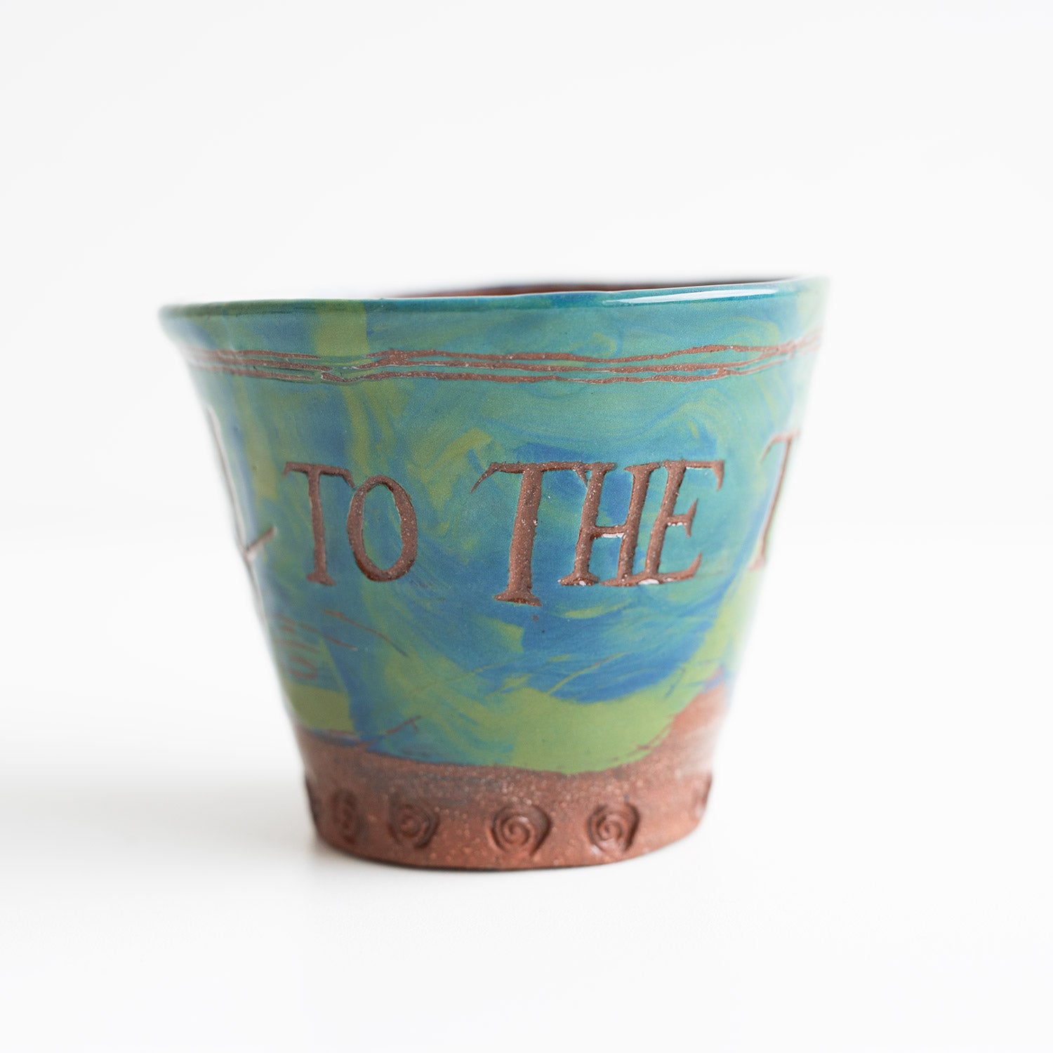 This is a close-up image of a small, decorative flower pot with the words "TO THE" written on it, featuring a swirled green and blue design, against a plain background.