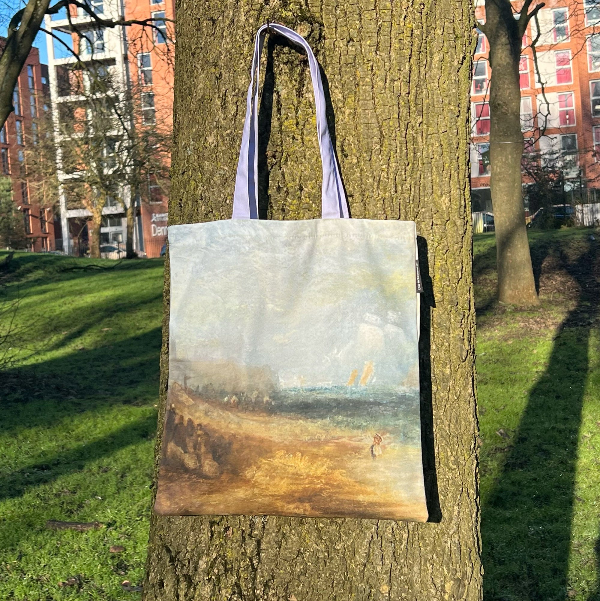 Tote bag featuring JMW Turner's watercolour titled Off Margate Pier. The bag is hanging on a tree in the Whitworth Park.