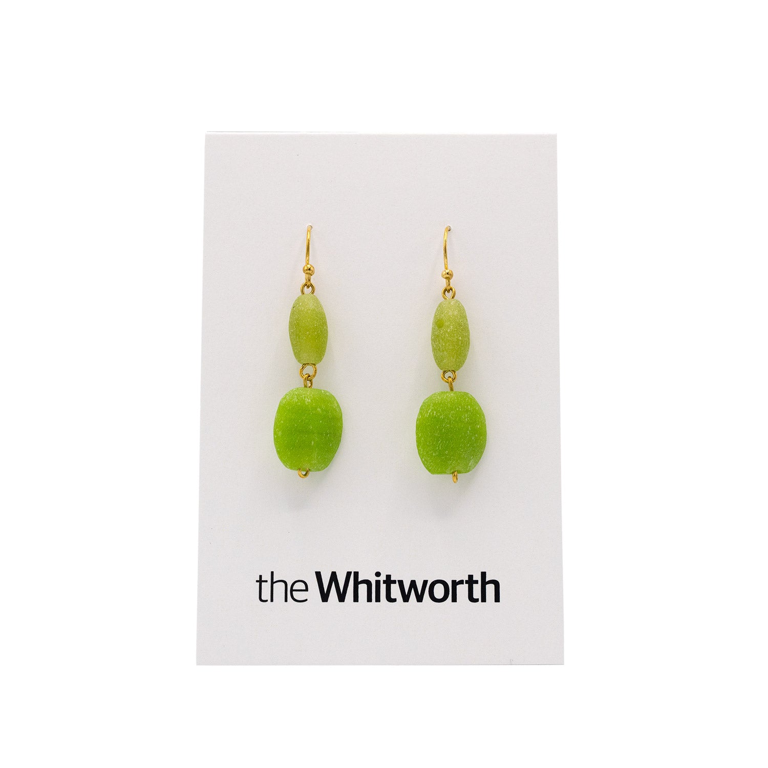 A pair of earrings with gold hooks, dark green cubes, and faceted light blue teardrop beads hang on a white card with the Whitworth logo.