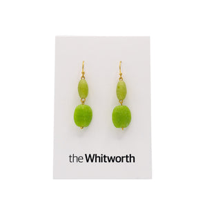 A pair of earrings with gold hooks, dark green cubes, and faceted light blue teardrop beads hang on a white card with the Whitworth logo.