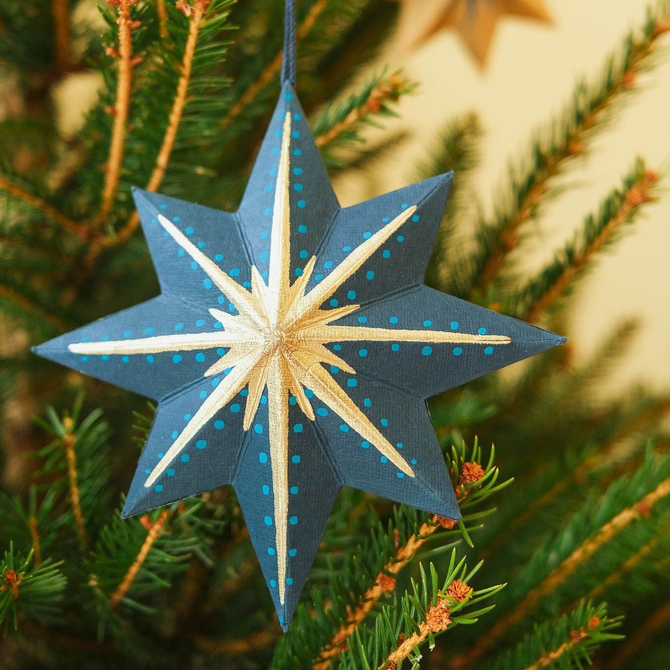 Blue and white star-shaped ornament hanging on a Christmas tree.