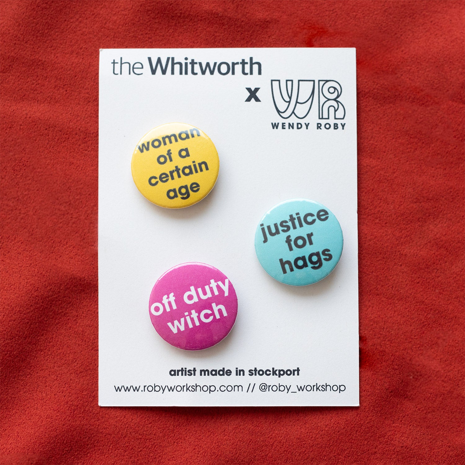 Three badges with feminist slogans presented on white backing card and a red fabric background.