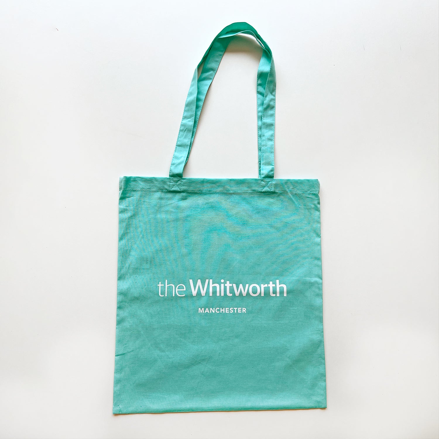 Mint coloured tote bag with Whitworth logo against white background.
