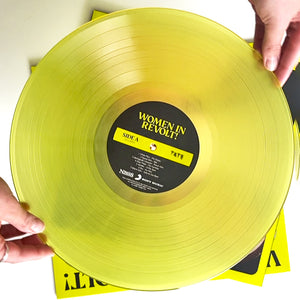 A person holding a bright yellow vinyl record for Women in Revolt. The photograph is taken from above.