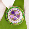 Pin with a purple flower design and 'Women's Suffrage' text on a green shirt.