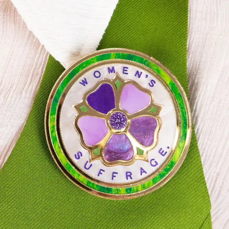 Pin with a purple flower design and 'Women's Suffrage' text on a green shirt.