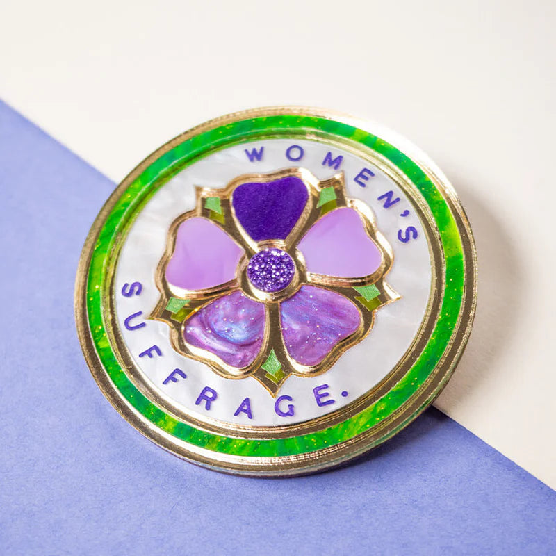 Pin with purple flower design and 'Women's Suffrage' text on a white and blue background