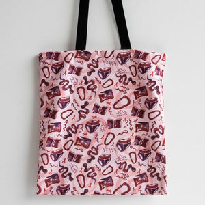 Tote bag hung against white backdrop. The textiles are printed with Sarah-Joy Ford's A Queer Manifesto print. Pink, purple and red textile design