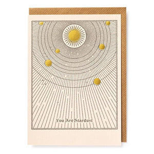 Card, kraft paper envelope. White and gold print with a sun in the middle and planets. Text reads you are stardust.