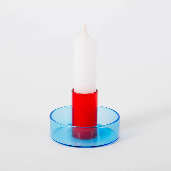 White background shot of the red and blue duo tone glass candle holder with a white candle in it.