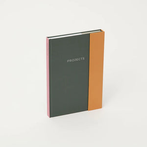 The green and orange notebook standing on the narrow edge and seen at a slight angle.