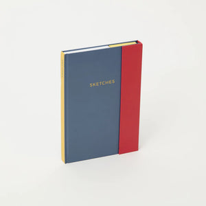 The dove grey and red notebook standing on the narrow edge and seen at a slight angle.