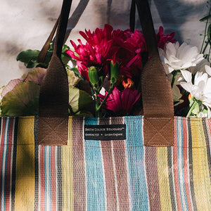 Lifestyle shop of a brown striped bag with some flowers inside.