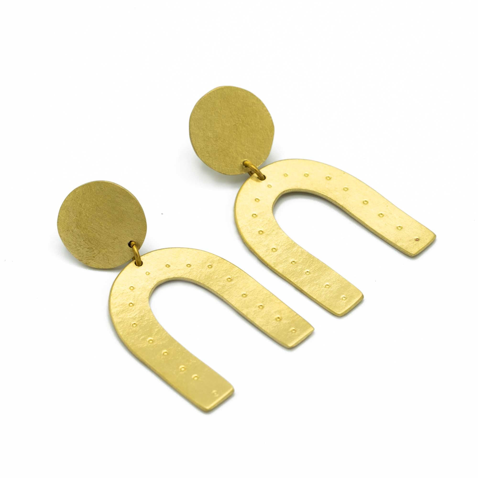 Stood earrings made from brass in the shape of an arch. White background.