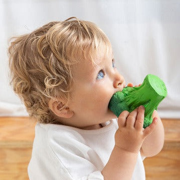 A small child holding a brocolli shaped baby teether in thier mouth.