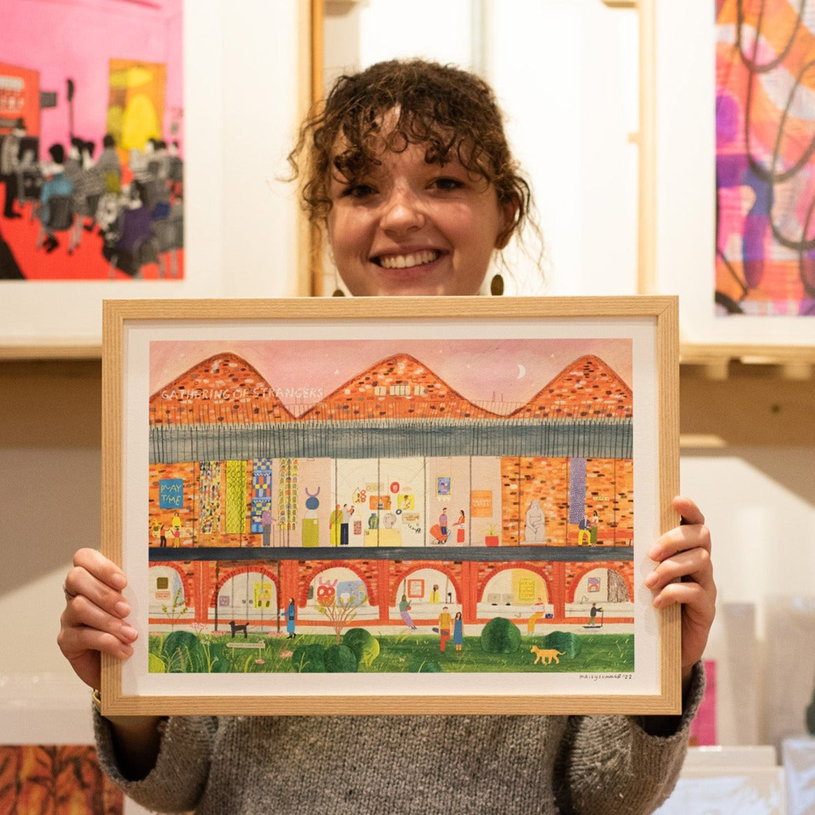 Portrait of Maisy Summer holding her print in front of other prints at the Whitworth