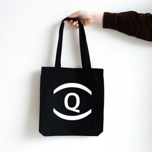 A person holding a black tote bag with the UnDefining Queer exhibition logo. White background.