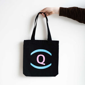 A person holding a black tote bag with the UnDefining Queer exhibition logo. White background.